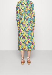 Blommig maxiklänning med långa ärmar, som har ett livfullt mönster i blått, gult, rosa och grönt, en dragkedja i ryggen och en lätt svängig silhuett.