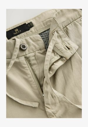 Beige vászon nadrág cipzárral és gombos záródással. Belső szövet részletekkel rendelkezik, geometrikus mintával és övéklyukakkal.