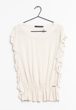 Jasno beżowa bluzka z falbaniastymi rękawami, elastycznym pasem i subtelnym wzorem. Wisi na czarnym haku na białym tle.