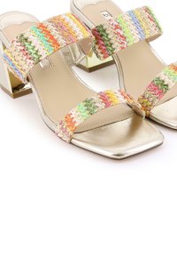 Tacones metálicos dorados con dos tiras trenzadas de varios colores. Diseño de punta cuadrada y tacón bajo. Textura suave en la plantilla.