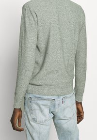 Suéter gris de punto con acabado texturizado, escote redondo y puños acanalados, combinado con vaqueros azul claro que tienen bolsillos traseros.