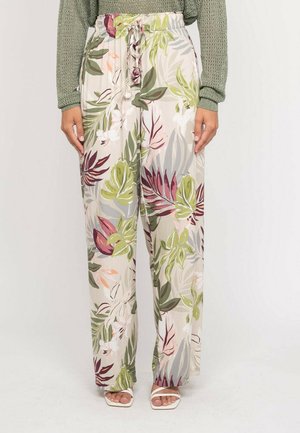Pantalon ample à taille haute avec un fond beige et un imprimé de feuilles tropicales vertes, roses et violettes, porté avec des sandales blanches et un pull en maille vert.