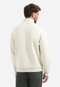 Crème-kleurige sweater met een hoge kraag, ontspannen pasvorm, ribbels aan de manchetten en de zoom. De stof heeft een gladde textuur, geschikt voor casual gebruik.