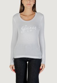 Camisa de manga larga en gris claro con un escote redondo y el logo "Guess" con acentos de rhinestones. Tejido suave con una silueta ajustada.
