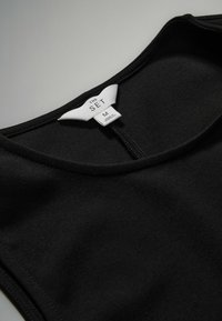 Zwart mouwloos top met een ronde halslijn, een gladde textuur en een label met de tekst "THE SET" maat M, weergegeven tegen een neutrale achtergrond.