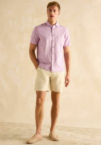 Kerge roosa lühikeste varrukatega särk, beežid lühikesed püksid ja pruunid libisevad kingad. Tähtsad detailid: nööpide sulgemine, rinna tasku ja vaba lõige.