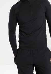 Svart, långärmad träningsskjorta med halvdragkedja och raglanärmar, tillverkad av ett mjukt och stretchigt material. Minimalistisk design.