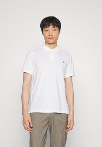 Hvid polo shirt lavet af bomuld, med en klassisk krave, korte ærmer og et lille logo på venstre bryst. Enkel, glat tekstur.