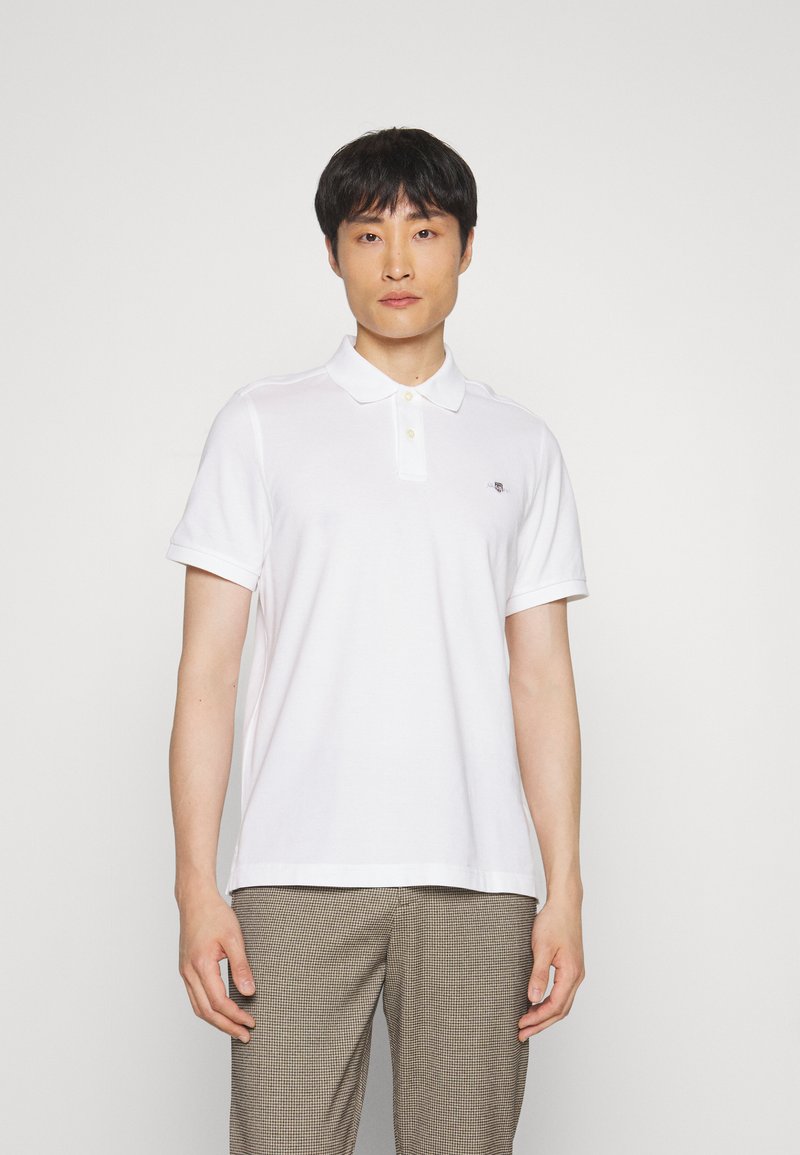 Hvid polo shirt lavet af bomuld, med en klassisk krave, korte ærmer og et lille logo på venstre bryst. Enkel, glat tekstur.