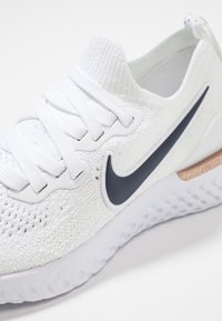 White knit sneaker featuring a dark gray Nike swoosh, textured upper, flat laces, and a lightweight, cushioned sole with a slight accent.