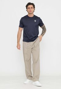 T-shirt a maniche corte di colore navy con un piccolo logo sul petto, abbinato a pantaloni cargo beige chiaro e sneakers bianche. Tessuto morbido, vestibilità rilassata.