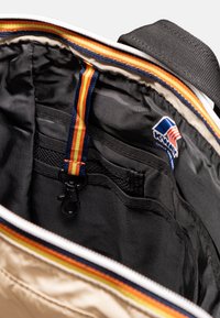Interno della borsa beige con tessuto nero, presenta bordi a righe multicolori, ganci e tasche organizzative. Logo K-Way visibile.