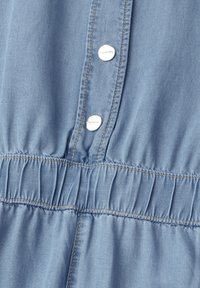 Lyseblåt denimplagg med elastisk talje med rynker og to sølvfarvede trykknapper mærket "Street One" på frontklappen.