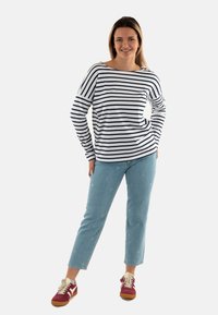 Camicia a maniche lunghe a righe bianca e blu navy, con vestibilità rilassata. Abbinata a jeans azzurri chiari con ricamo floreale e sneaker bordeaux.