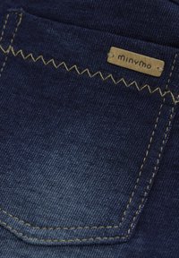 Denim w ciemnoniebieskim kolorze, z tylną kieszenią, żółtym przeszyciem i małą brązową metką z napisem "minymo."