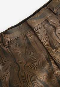 Gros plan d’un tissu brun et noir à motif ondulé avec passants de ceinture et coutures ajustées, probablement partie d’un vêtement.