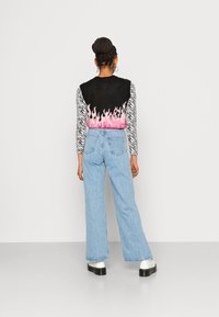 Sweater com padrão de chamas pretas e rosas sobre uma camisa de mangas longas com padrão de zebras, combinado com jeans de cintura alta em azul claro e botas pretas robustas.