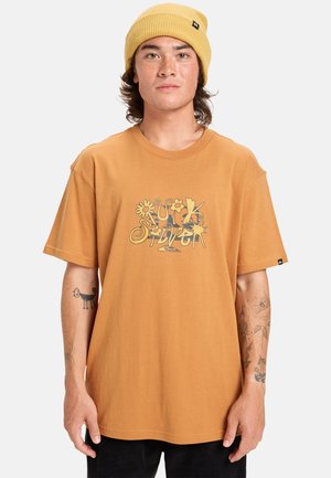 T-shirt en coton marron avec un graphique floral coloré. Coupe décontractée avec des manches courtes. Le porteur porte un bonnet en tricot jaune et a des tatouages visibles.