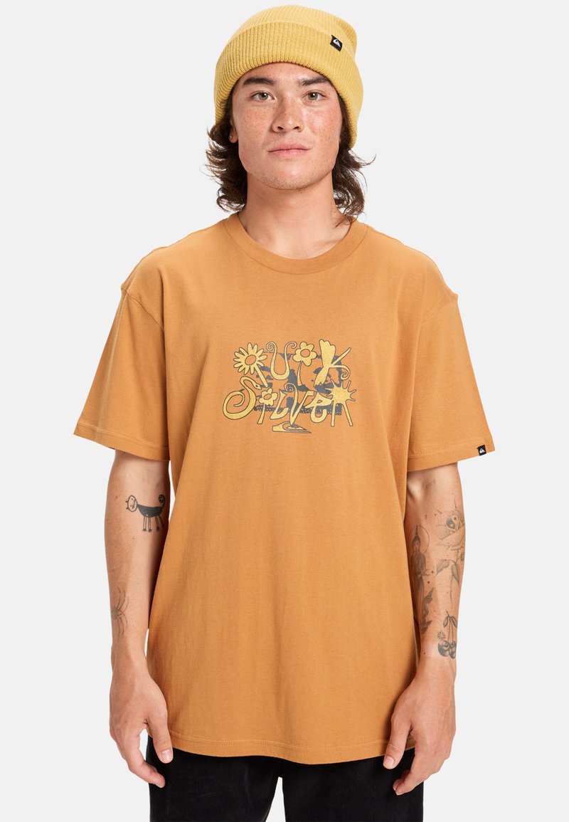 Bruine katoenen t-shirt met een kleurrafloriemotief. Ontspannen pasvorm met korte mouwen. De drager heeft een gele gebreide muts en zichtbare tatoeages.