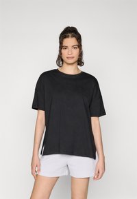 Crna oversized majica kratkih rukava s suptilnim teksturiranim uzorkom. Uparen s svijetlosivim šorcem.