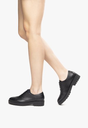 Scarpe in pelle nera stringate con design brogue, caratterizzate da punta arrotondata, dettagli testurizzati e suola spessa con tacche.