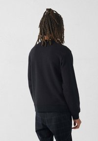 Sweatshirt noir avec col rond, poignets et ourlet côtelés. Tissu doux avec une coupe décontractée, associé à un pantalon à carreaux sombres. Vue de dos.