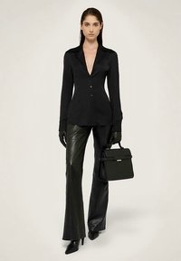 Camisa negra abotonada con escote en V profundo, combinada con pantalones acampanados de cuero negro, guantes y un bolso estructurado. Textura lisa, diseño elegante.