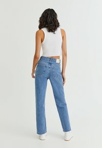 Jeans bleu clair avec une coupe taille haute, des jambes droites et décontractées, et un ourlet effiloché. Comprend des poches arrière et une étiquette blanche à la ceinture.