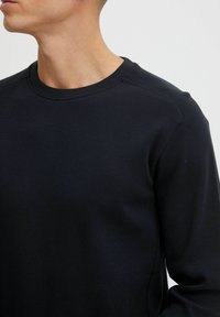 Chemise à manches longues bleu marine avec un tissu texturé, un col rond et des détails de couture subtils le long des coutures des épaules.