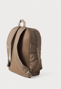 Ruda audinio kuprinė apvalios formos, su tinklinėmis šoninėmis detalėmis, užtrauktuko uždarymu, reguliuojamomis paminkštintomis petnešomis ir viršutine nešimo rankena.