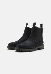 Bottines en suède noir avec des panneaux élastiques sur les côtés et des languettes de traction. Elles sont dotées d'une semelle en caoutchouc robuste avec un motif texturé pour une bonne adhérence.