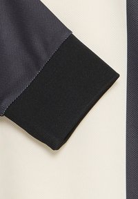 Langærmet beklædningsgenstand med en sort ribbet manchet, grå paneler med et struktureret mønster og en cremefarvet krop.