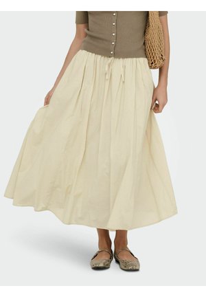 Femme portant un haut beige boutonné, une jupe midi fluide couleur crème, des ballerines à motif serpent, et un sac fourre-tout tressé.