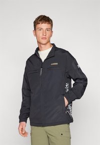 Chaqueta negra con cremallera y dos bolsillos frontales, puños elásticos y un parche de logo. Presenta un detalle con un patrón a lo largo del lado.