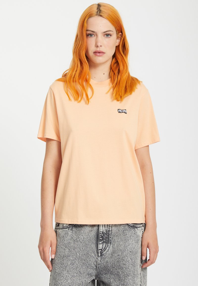 Short-sleeve peach t-shirt made of soft cotton, featuring a small black logo on the left chest, with a relaxed fit.