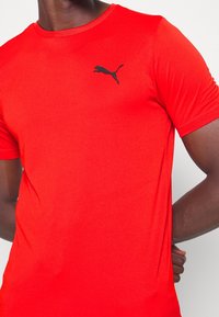 Camiseta deportiva corta roja de manga corta hecha de un tejido suave, con un logo negro de Puma en el área izquierda del pecho y un escote redondo.