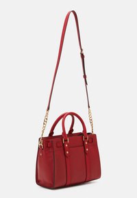 Sac à main en cuir rouge avec finition texturée, doubles poignées, bandoulière en chaîne amovible, accents en métal doré et détails de coutures verticales.