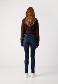 Dark blue skinny jeans with a high waist and two back pockets, paired with a textured brown knitted sweater. Smooth fabric and fitted design.