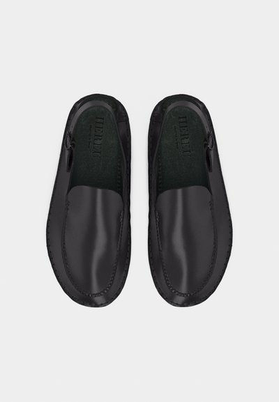 Mocassins en cuir noirs sans lacets avec bouts arrondis et détails de couture, vus de dessus sur un fond clair uni.