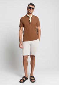 Bruine polo, beige shorts en zwarte sandalen. Een lichte sjaal om de nek voegt detail toe. De outfit heeft een casual zomerlook.
