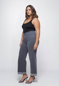 Grijze hoog-waisted jeans met opgerolde pijpen, gecombineerd met een zwarte aansluitende tanktop en zwarte hakken met bandjes. Gladde denim textuur.