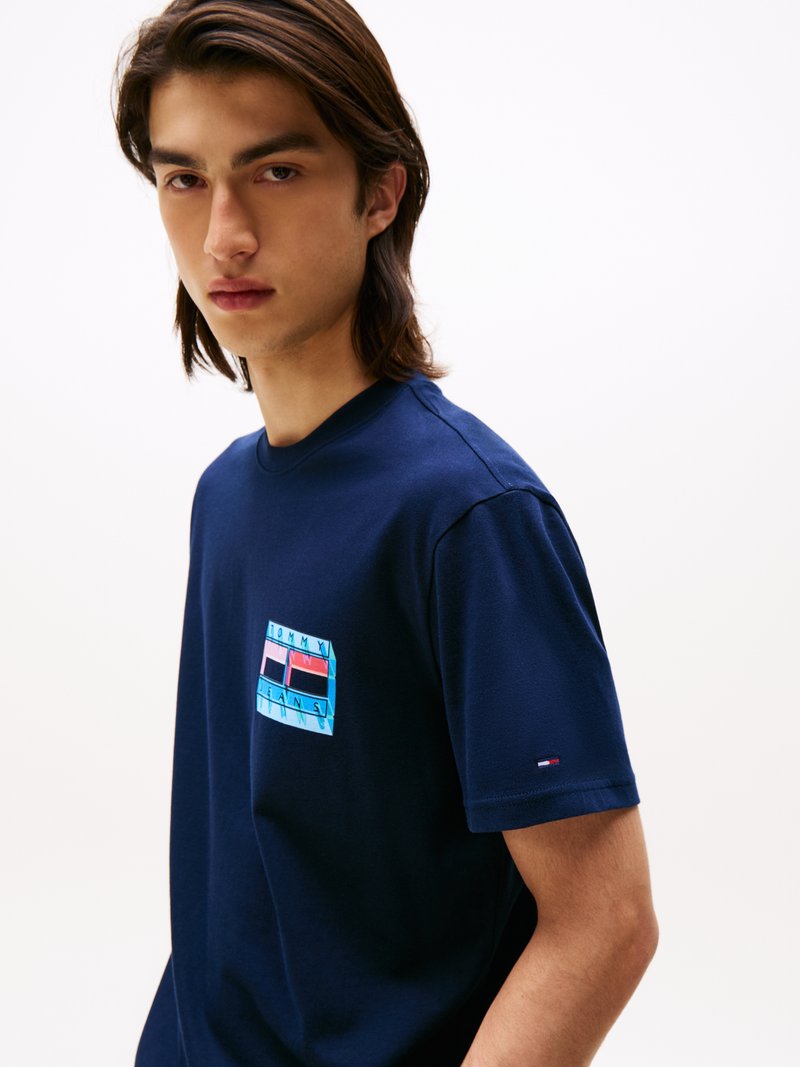 Camiseta de algodón azul marino con un parche de logo colorido que presenta patrones geométricos en el lado izquierdo del pecho. Mangas cortas y cuello redondo.