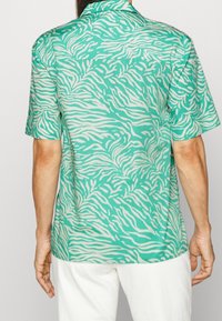Chemise à manches courtes en turquoise avec des rayures blanches en zèbre. Elle possède un col classique et une coupe décontractée, fabriquée à partir d'un tissu léger.