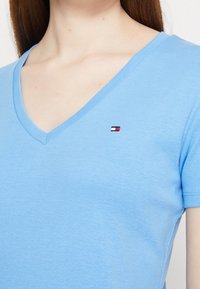 Světle modré tričko s výstřihem do V vyrobené z měkké tkaniny, s malým vyšívaným logem na levé straně hrudi. Krátké rukávy, slim fit.
