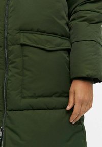 Groene pufferjas met een ritsluiting, grote voork pocket en geweven stof met een gladde afwerking. De manchetten zijn elastisch voor een goede pasvorm.