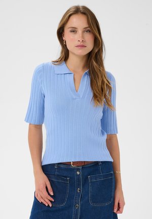 Hele sinine, ribidega lühikeste varrukatega polo särk, millel on v-kaelus ja struktuurne krae. Kandmiseks koos teksaseelikuga, millel on esiküljel nööbid ja taskud.