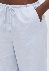 Light blue linen pants with an elastic waistband and drawstring, featuring side pockets and a smooth texture.