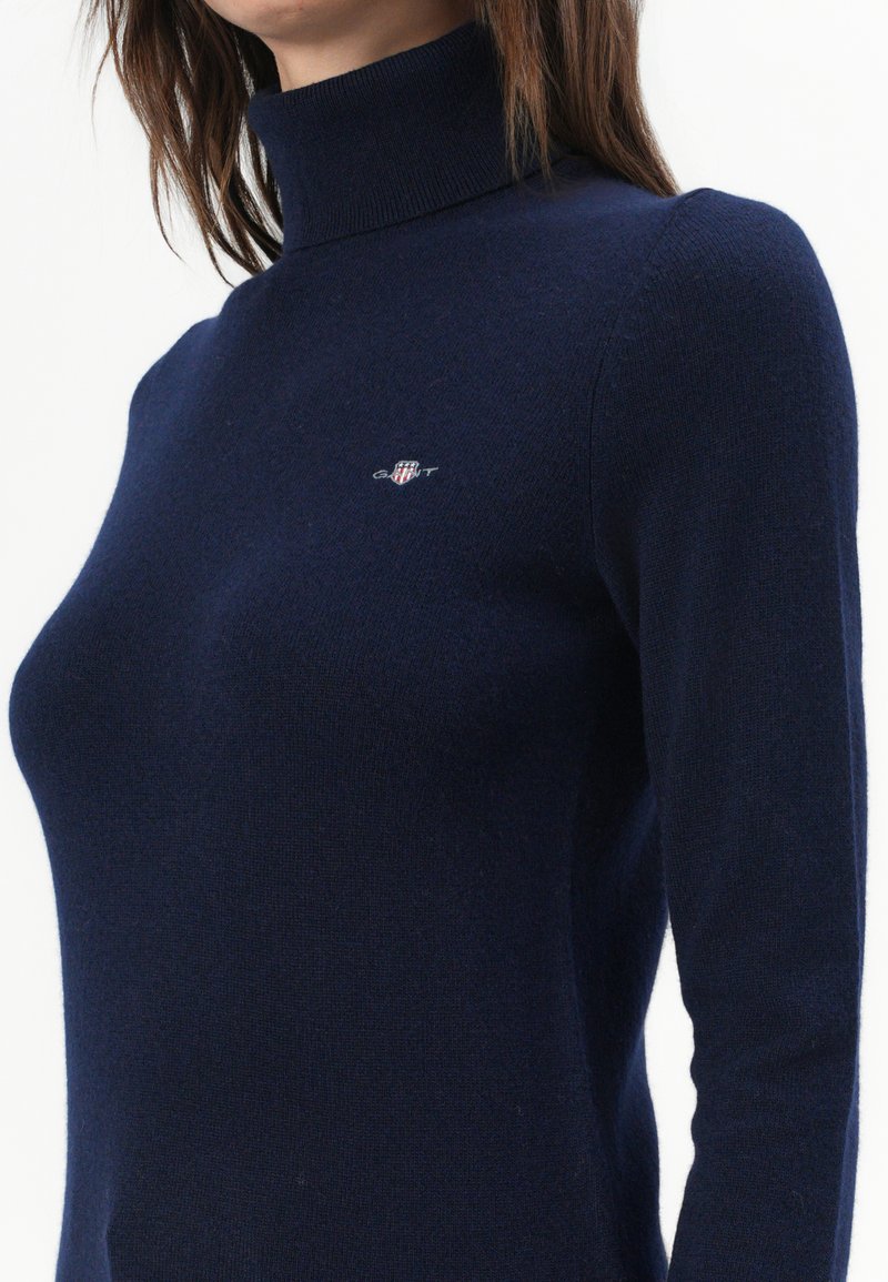 Dunkelblaues Rollkragenpullover aus weichem Strickmaterial, mit einem kleinen gestickten Logo auf der Brust und passender Silhouette.