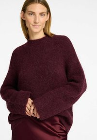 Bordeauxstickad tröja med en mjuk, strukturerad yta, med hög hals och överdimensionerade ärmar. Matchas med en satängkjol i bordeaux.
