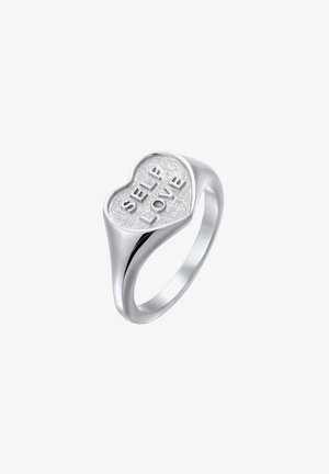 Zilveren hartvormige ring met een gestructureerd oppervlak, gegraveerd met "ZELF LIEFDE" in vette letters. Gladde band gaat over in het hartontwerp.